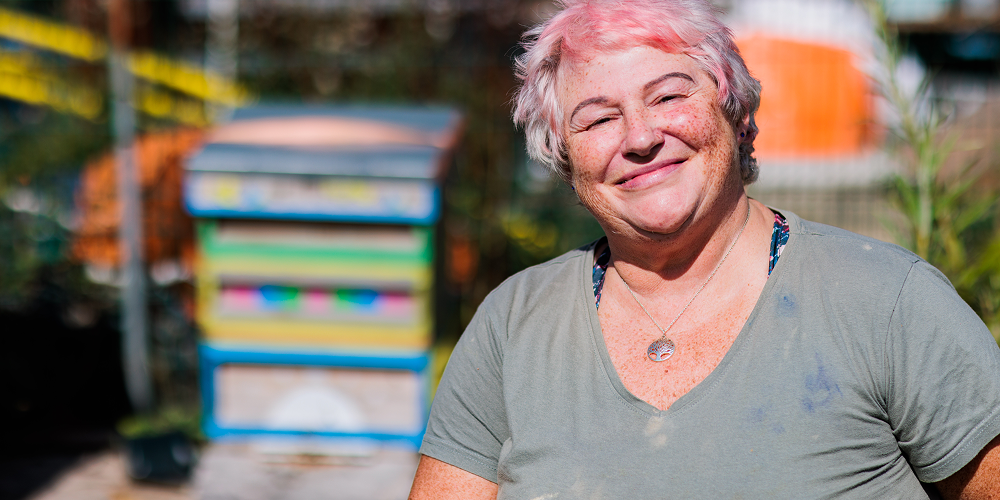 A woman with pink hair smiling towards the camera in a garden. 