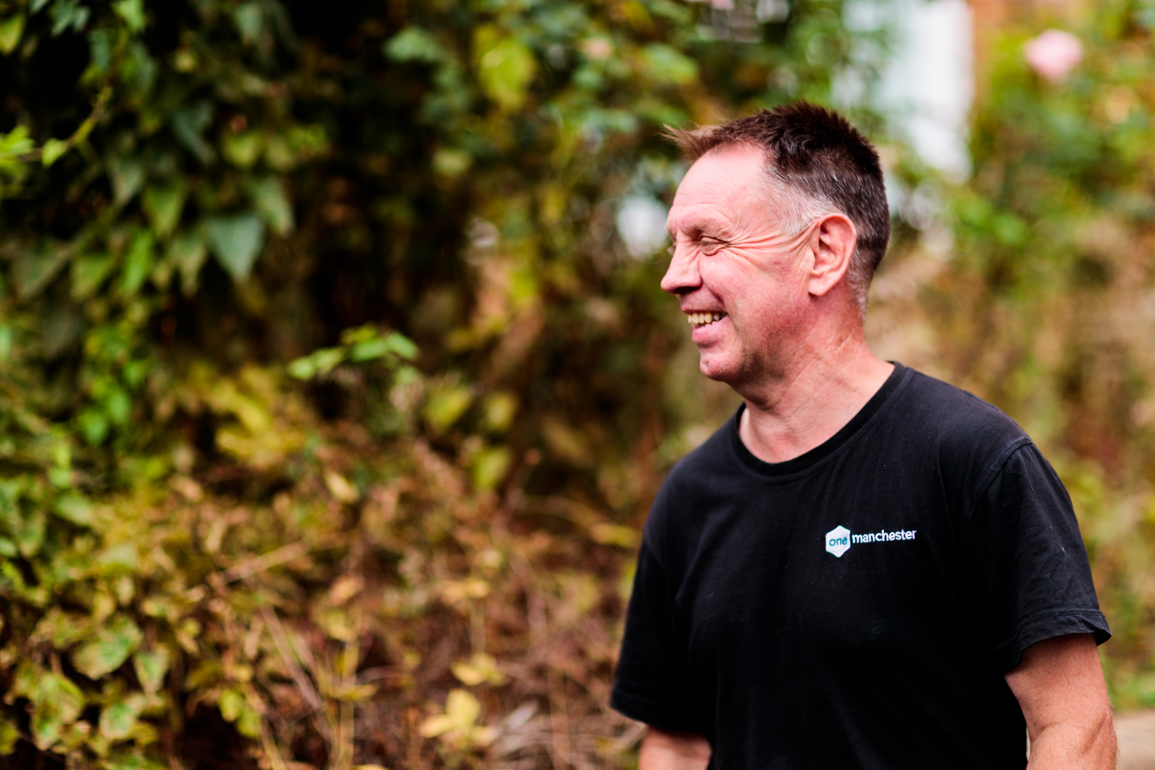 A man smiling while working outside, wearing a One Manchester uniform.