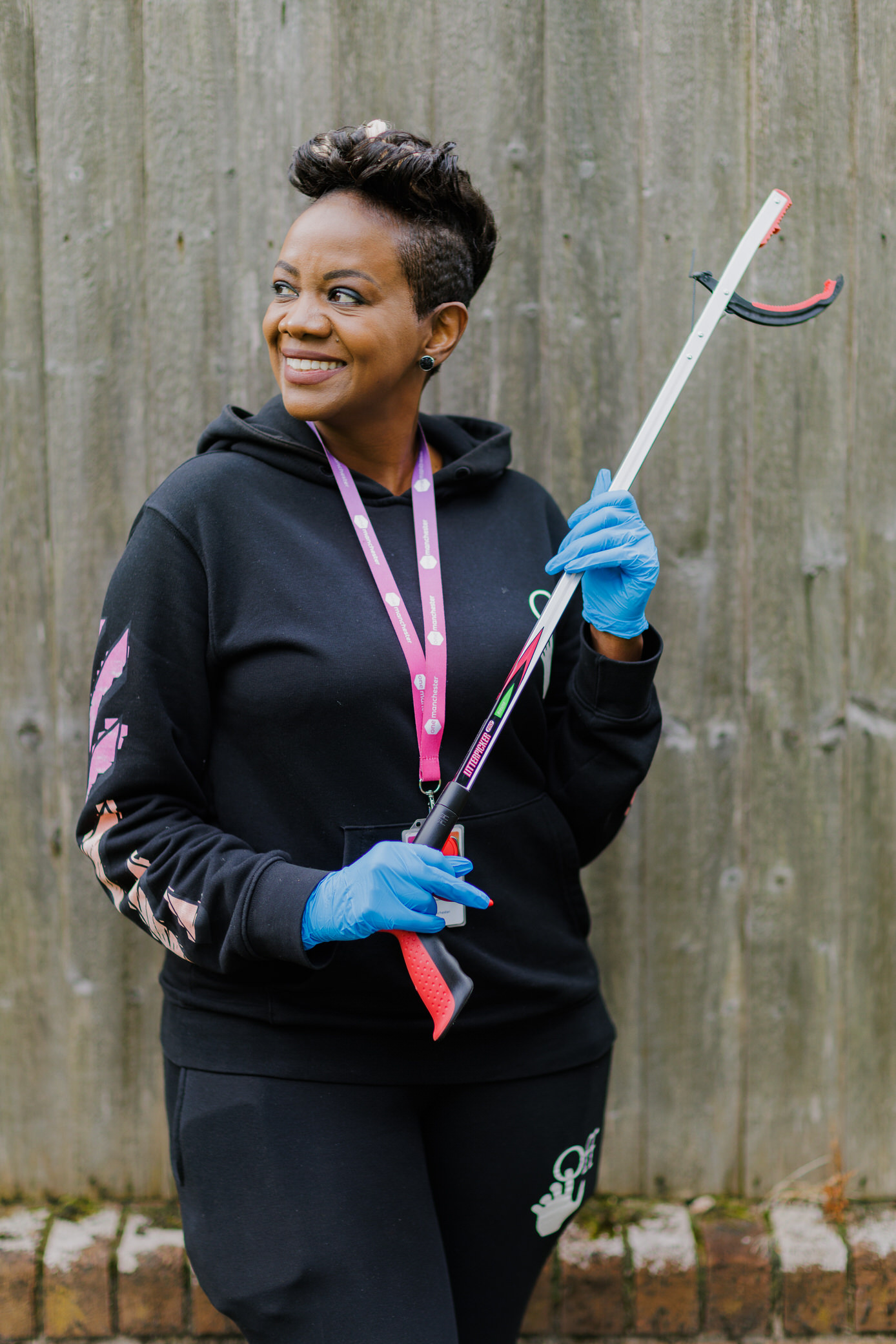 One Manchester female colleague holding a litter picker in front of a fence.