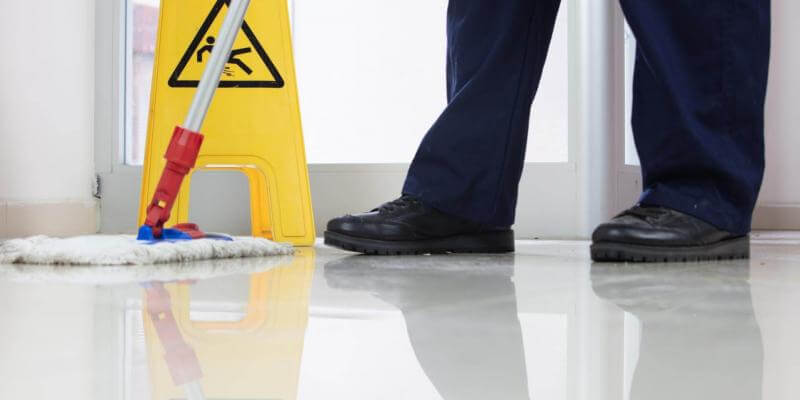 Photo of person mopping a floor with a wet floor sign next to them