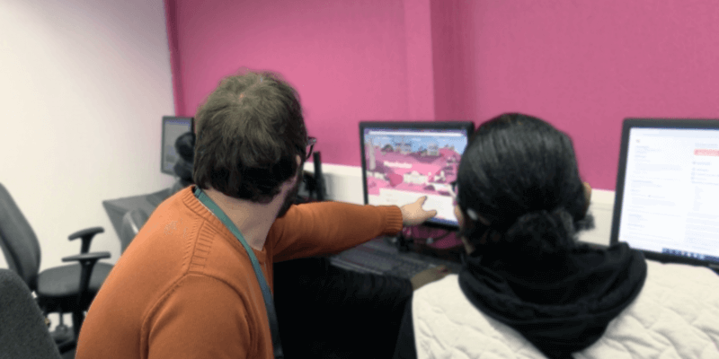 Two people sitting at a computer in a pink room