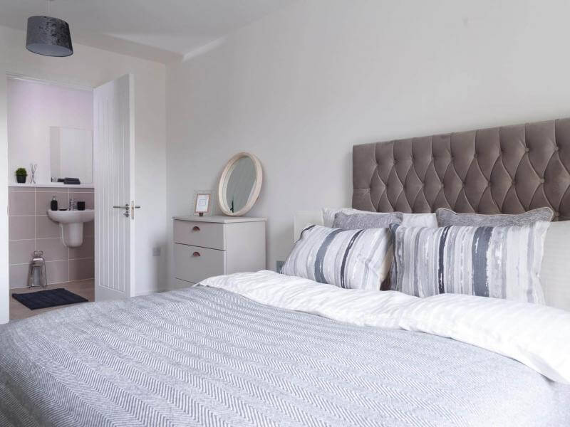 Photo of a bedroom at The Clockworks with a bed and set of drawers, the en suite is visible through the open door