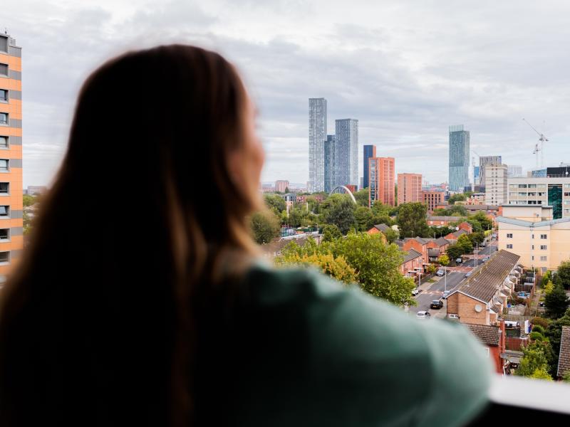 A woman looking out over the landscape of Manchester from a high rise building.