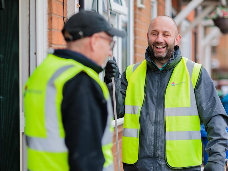 Two men wearing high visibility jackets sat stood outside a property in Manchester having a conversation.