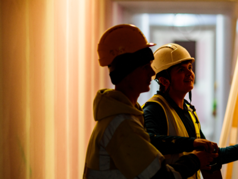 Two people doing building work wearing high vis and builders hats.