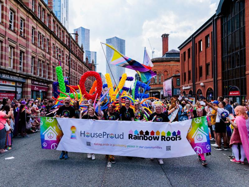 An image of HouseProud and One Manchester colleagues marching in rainbow costumes in the Manchester Pride Parade