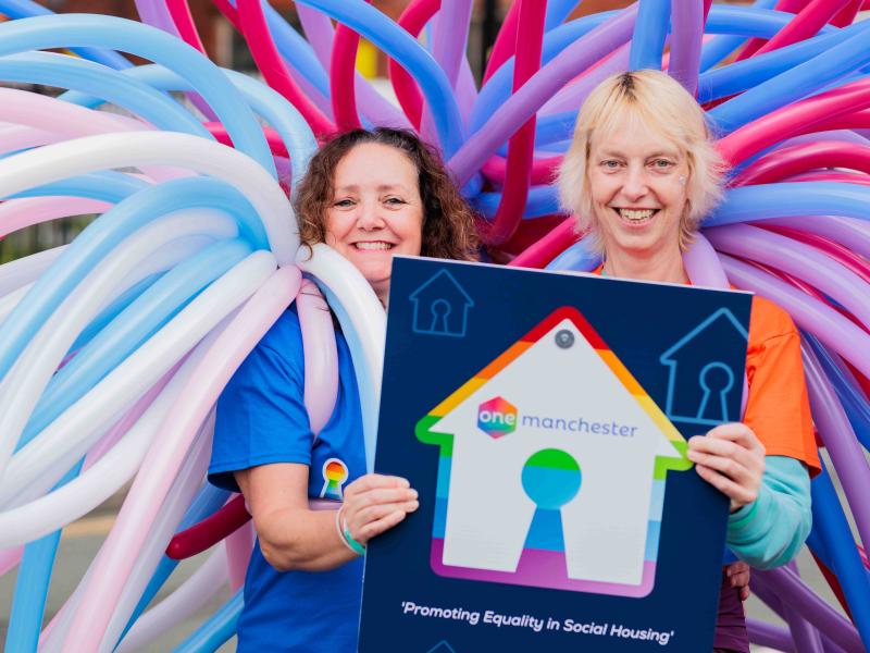 One Manchester colleagues dressed in pride outfits holding a HouseProud and One Manchester sign which reads Promoting equality in social housing