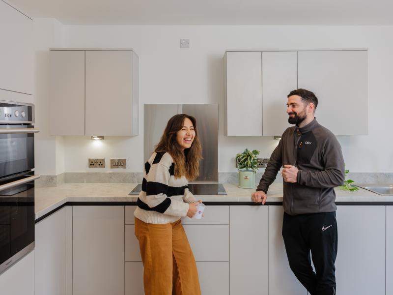 Woman laughing whilst chatting to man in a kitchen over a cup of tea