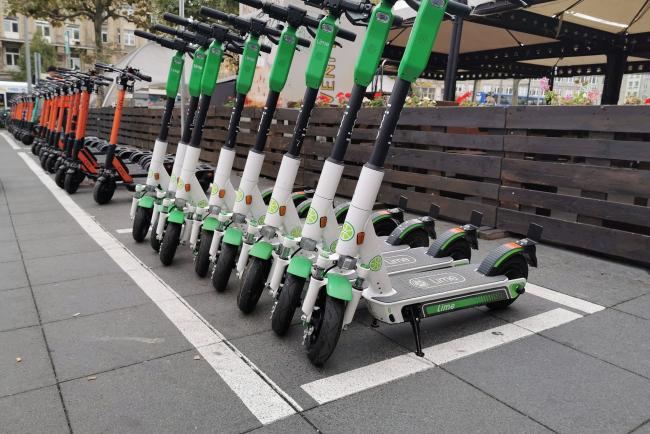 A picture containing a row of electric scooters on the pavement.