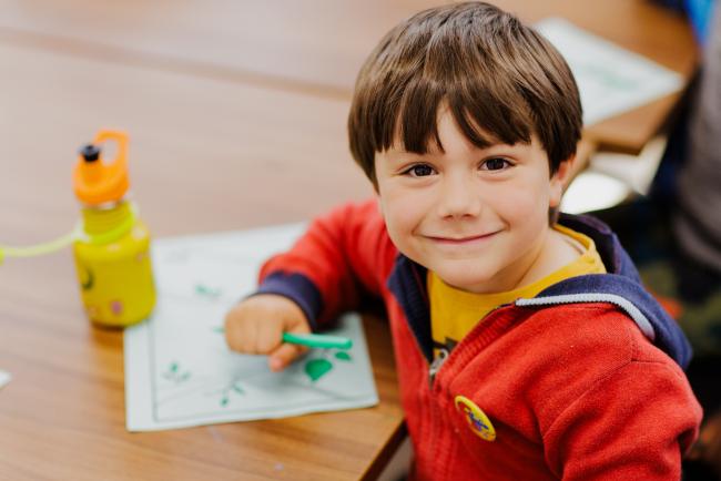 A small child wearing a red jumper, facing the camera and smiling.