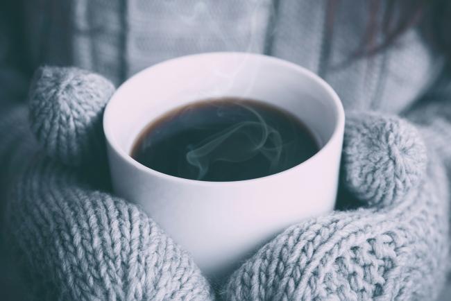 Close up of a person wearing mittens holding a cup