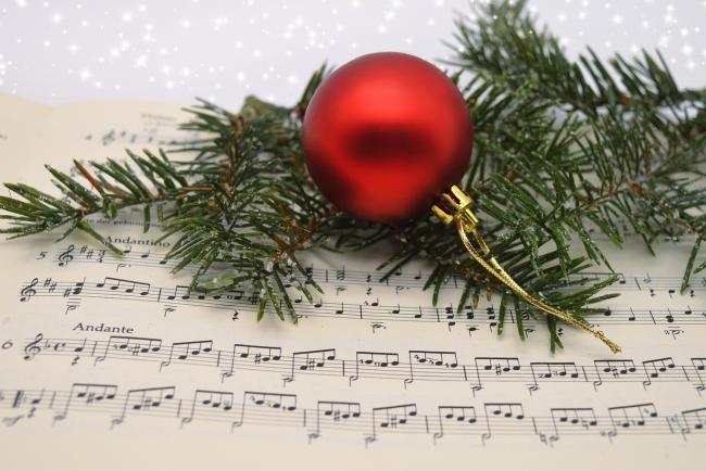 red christmas bauble on top of some fir tree branches on top of christmas carol sheet music