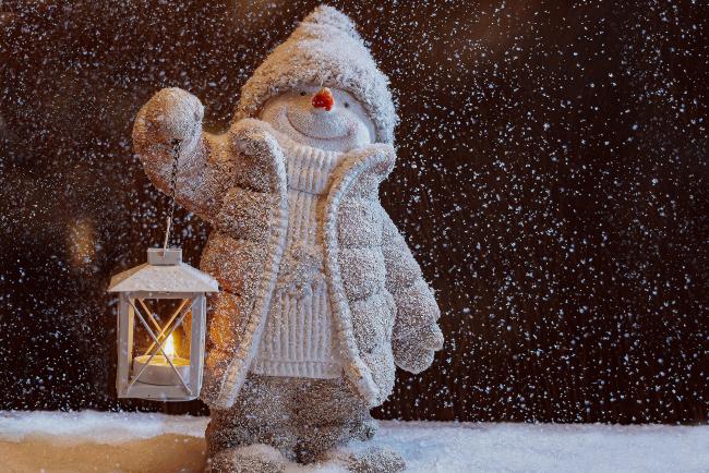 An image of a snowman ornament holding a lantern in the falling snow
